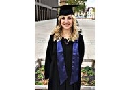 Masterabsolventin Christina Barth lächelt in klassischer Absolventenkluft mit Hut und Schal in die Kamera.
